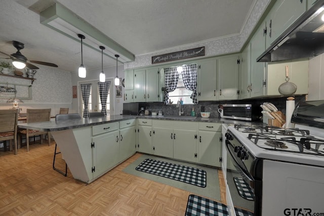 kitchen with under cabinet range hood, a peninsula, a sink, range with gas stovetop, and wallpapered walls