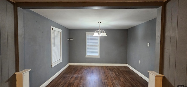 unfurnished dining area featuring dark wood-type flooring and a notable chandelier