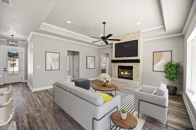 living room with a raised ceiling, a fireplace, dark wood-type flooring, and ceiling fan with notable chandelier