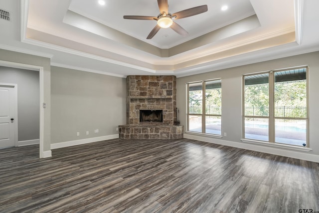 unfurnished living room with ornamental molding, ceiling fan, a fireplace, a raised ceiling, and dark wood-type flooring