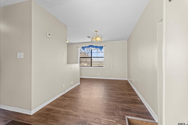 empty room featuring an inviting chandelier, baseboards, and wood finished floors