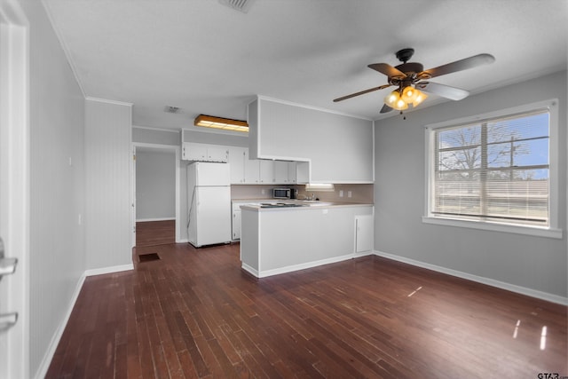 kitchen with a peninsula, stainless steel microwave, dark wood finished floors, and freestanding refrigerator