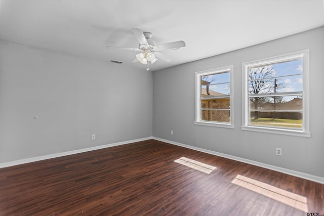 spare room with dark wood-style floors, baseboards, visible vents, and a ceiling fan