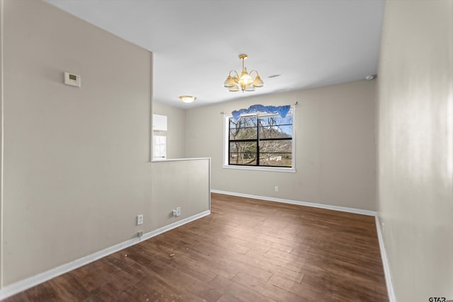 empty room with baseboards, wood finished floors, and a notable chandelier