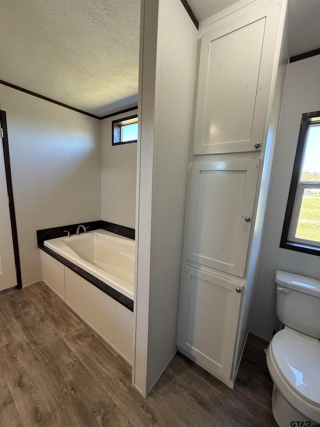 bathroom with a washtub, a textured ceiling, hardwood / wood-style flooring, and toilet