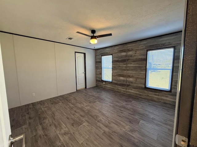 unfurnished bedroom with ceiling fan, dark hardwood / wood-style floors, wooden walls, and multiple windows