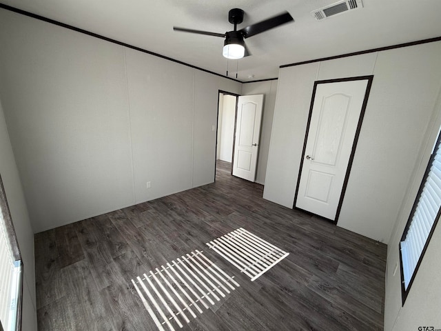 unfurnished bedroom featuring multiple windows, dark hardwood / wood-style flooring, ceiling fan, and crown molding