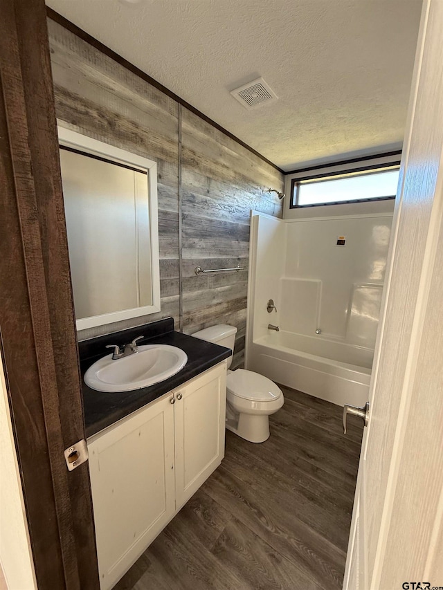 full bathroom featuring hardwood / wood-style floors,  shower combination, wooden walls, toilet, and a textured ceiling