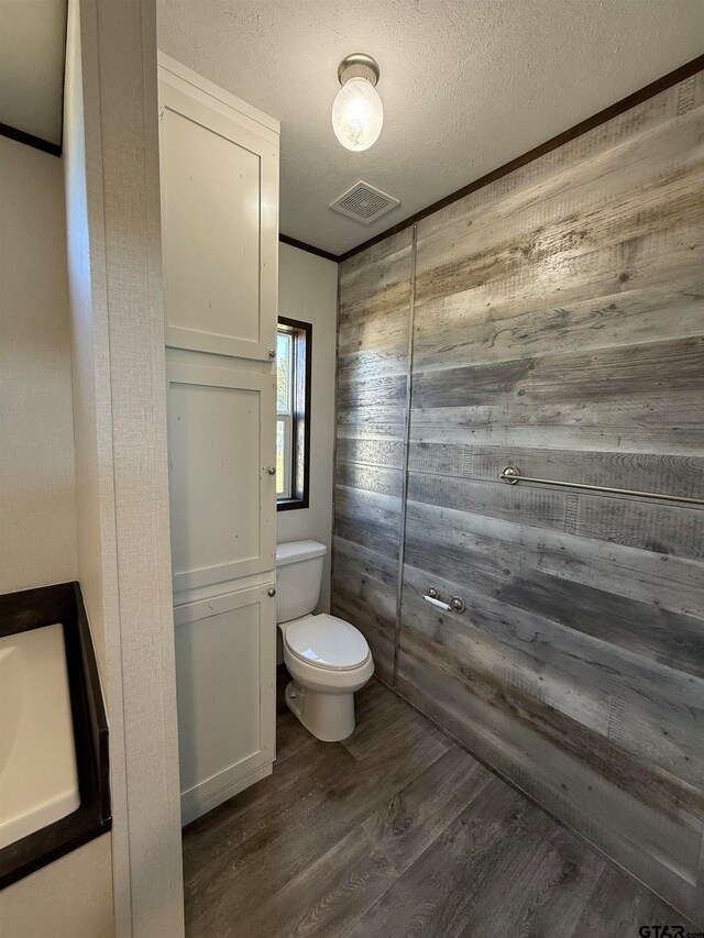 bathroom with wood walls, toilet, wood-type flooring, and a textured ceiling