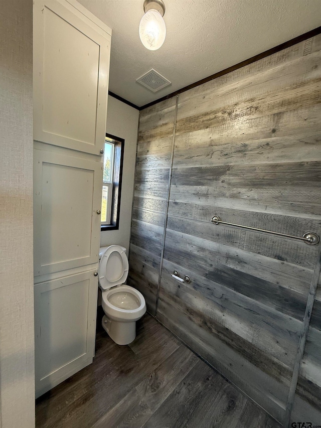 bathroom with wooden walls, toilet, a textured ceiling, and hardwood / wood-style flooring