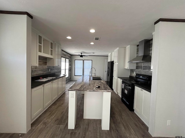 kitchen with black range with electric cooktop, sink, wall chimney range hood, a center island with sink, and fridge