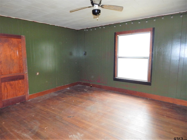 spare room with dark wood-type flooring, wood walls, and ceiling fan