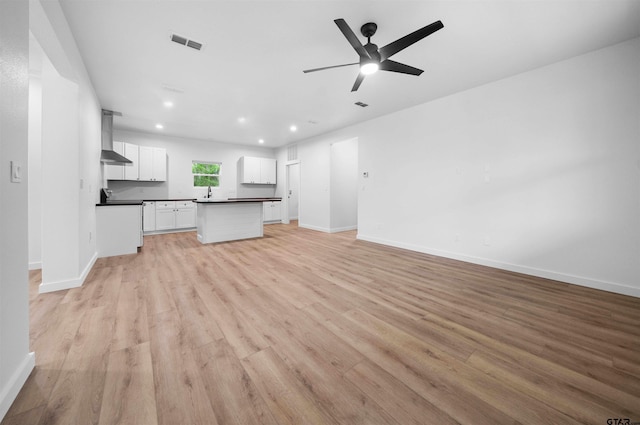 kitchen with visible vents, wall chimney exhaust hood, dark countertops, light wood-style floors, and open floor plan