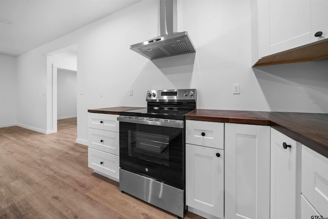 kitchen with stainless steel electric range, light wood finished floors, butcher block counters, white cabinets, and wall chimney exhaust hood