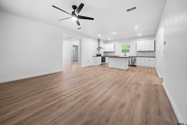 unfurnished living room featuring visible vents, baseboards, ceiling fan, a sink, and light wood-style floors