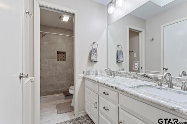 bathroom with tile patterned floors, toilet, a skylight, a tile shower, and vanity