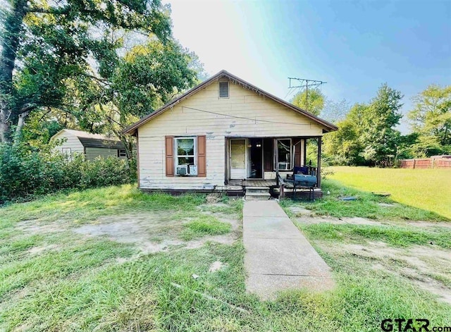 bungalow-style home featuring covered porch, a front yard, and a storage shed