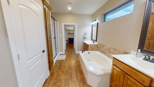 full bathroom with a bath, a sink, two vanities, a stall shower, and wood finished floors