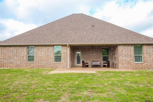 rear view of property featuring brick siding, roof with shingles, a patio, and a lawn