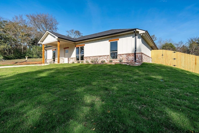 view of property exterior with a yard, brick siding, fence, and board and batten siding