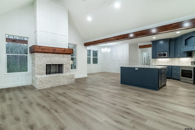 kitchen with stainless steel appliances, a kitchen island with sink, a fireplace, and light hardwood / wood-style flooring