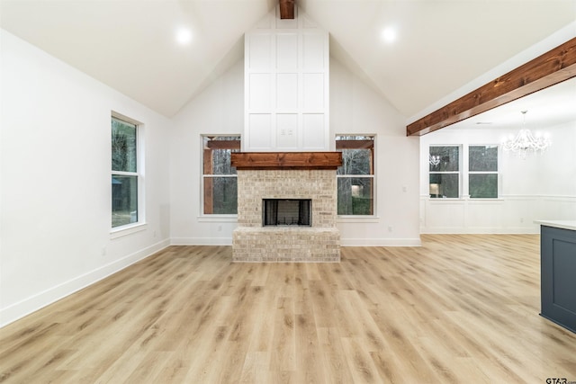 unfurnished living room with beam ceiling, high vaulted ceiling, light hardwood / wood-style floors, a brick fireplace, and a chandelier