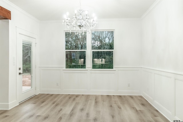 empty room with a notable chandelier, crown molding, and light wood-type flooring