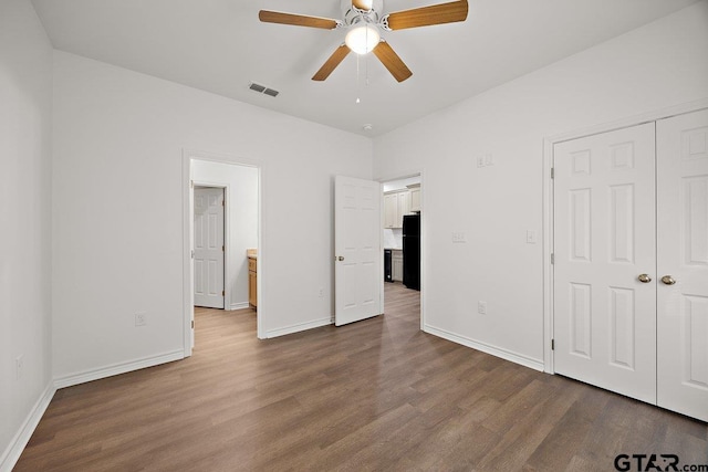 unfurnished bedroom featuring dark wood finished floors, a closet, visible vents, freestanding refrigerator, and baseboards