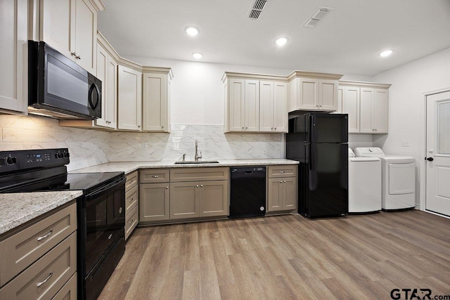 kitchen with a sink, black appliances, visible vents, and washer and dryer