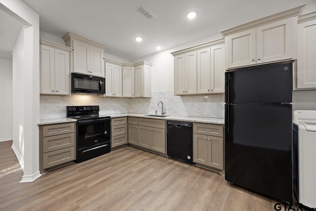 kitchen featuring a sink, visible vents, light wood-style floors, black appliances, and washer / dryer