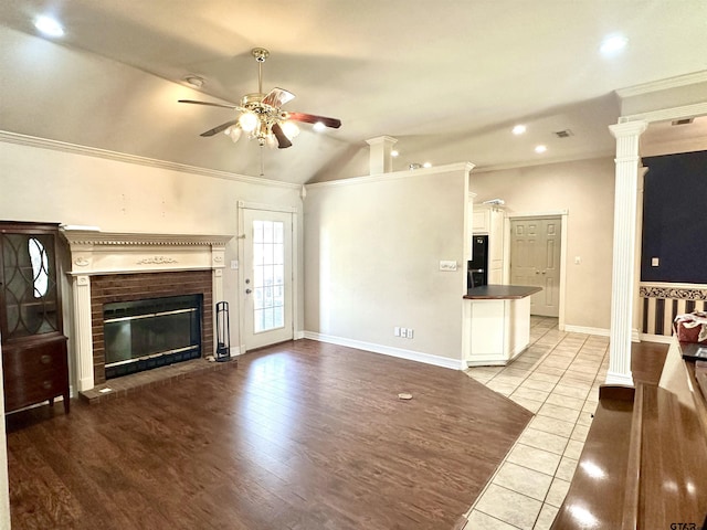 unfurnished living room featuring decorative columns, baseboards, ceiling fan, crown molding, and a brick fireplace