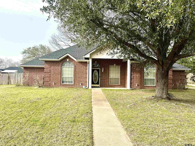 single story home featuring a shingled roof, a front yard, brick siding, and fence