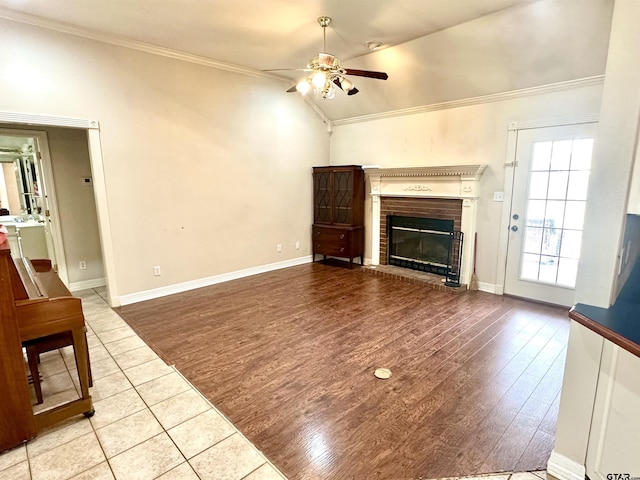 living area with a ceiling fan, ornamental molding, wood finished floors, vaulted ceiling, and a fireplace