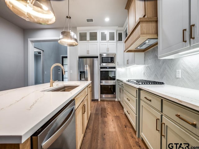 kitchen with stainless steel appliances, a center island with sink, sink, decorative light fixtures, and dark hardwood / wood-style flooring