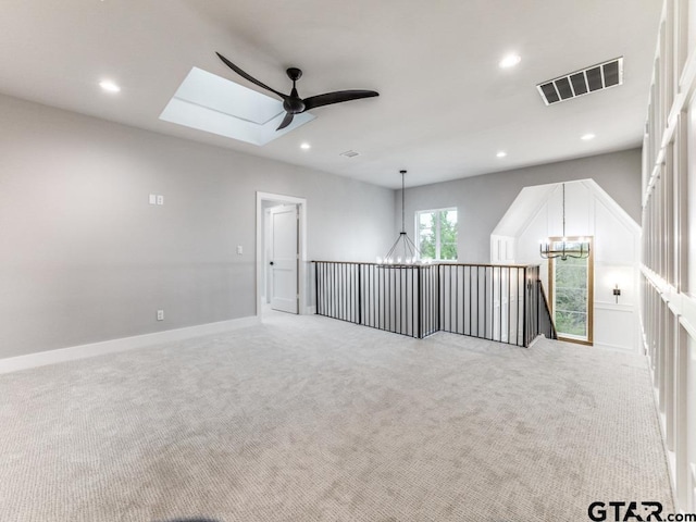 carpeted empty room featuring ceiling fan with notable chandelier and a skylight