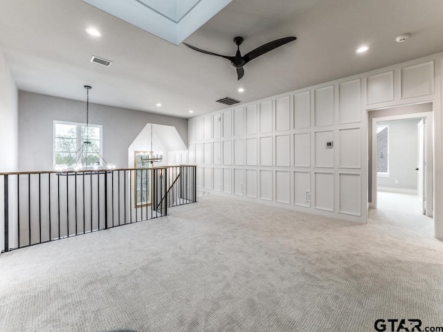 empty room featuring ceiling fan with notable chandelier and light carpet