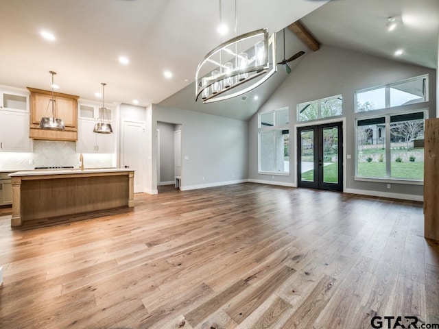 unfurnished living room featuring beamed ceiling, a chandelier, light wood-type flooring, and high vaulted ceiling