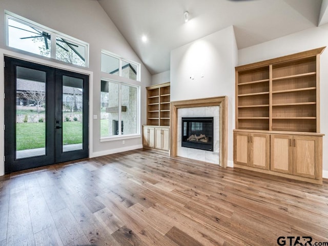 unfurnished living room with a tiled fireplace, french doors, plenty of natural light, and light hardwood / wood-style floors