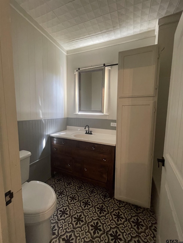 bathroom featuring crown molding, vanity, wood walls, and toilet