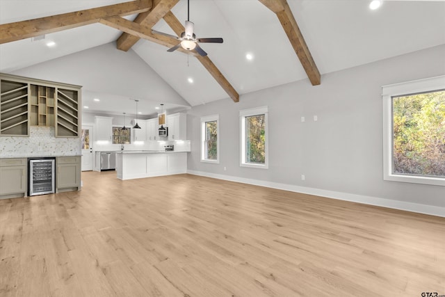 unfurnished living room featuring a wealth of natural light, beam ceiling, wine cooler, and light hardwood / wood-style flooring