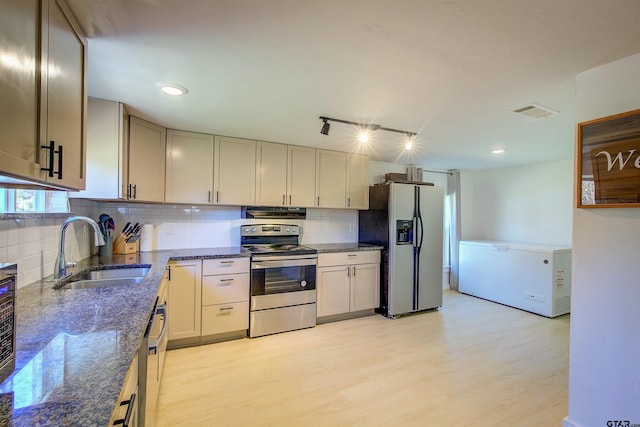 kitchen featuring decorative backsplash, appliances with stainless steel finishes, sink, light hardwood / wood-style flooring, and dark stone countertops