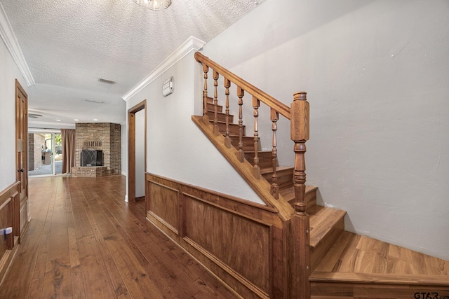 stairway with a fireplace, crown molding, hardwood / wood-style floors, and a textured ceiling