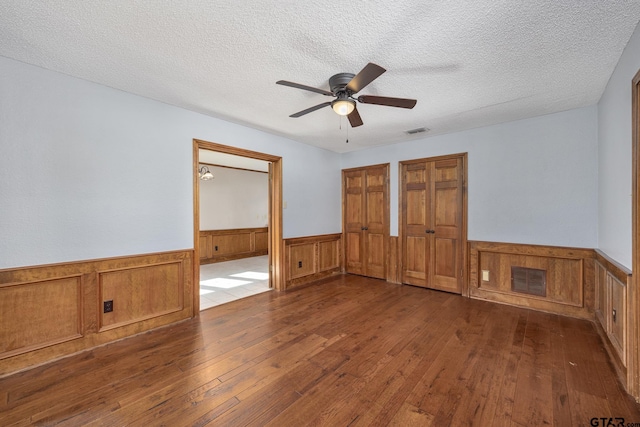 empty room with a textured ceiling, ceiling fan, and dark hardwood / wood-style floors