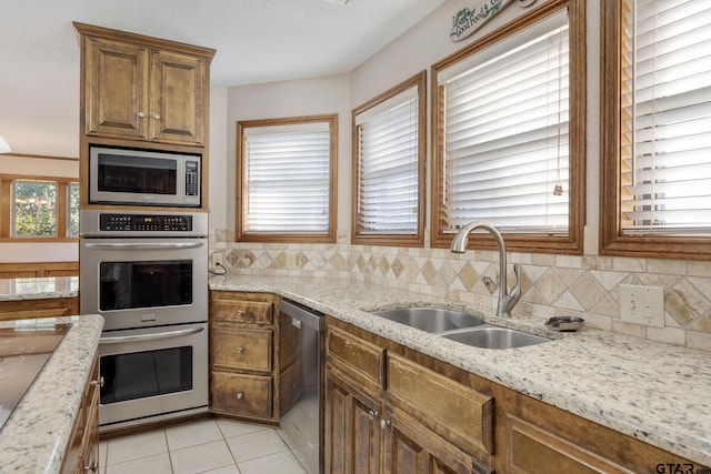 kitchen featuring light stone countertops, sink, decorative backsplash, light tile patterned floors, and appliances with stainless steel finishes