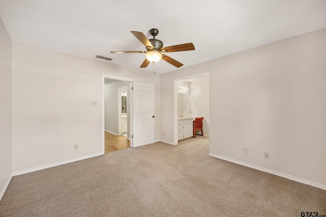 unfurnished bedroom with a textured ceiling, ceiling fan, ensuite bathroom, and light carpet