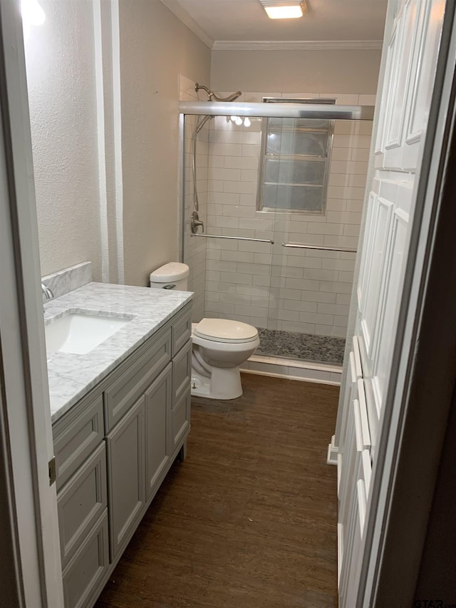 full bath featuring a stall shower, toilet, wood finished floors, ornamental molding, and vanity