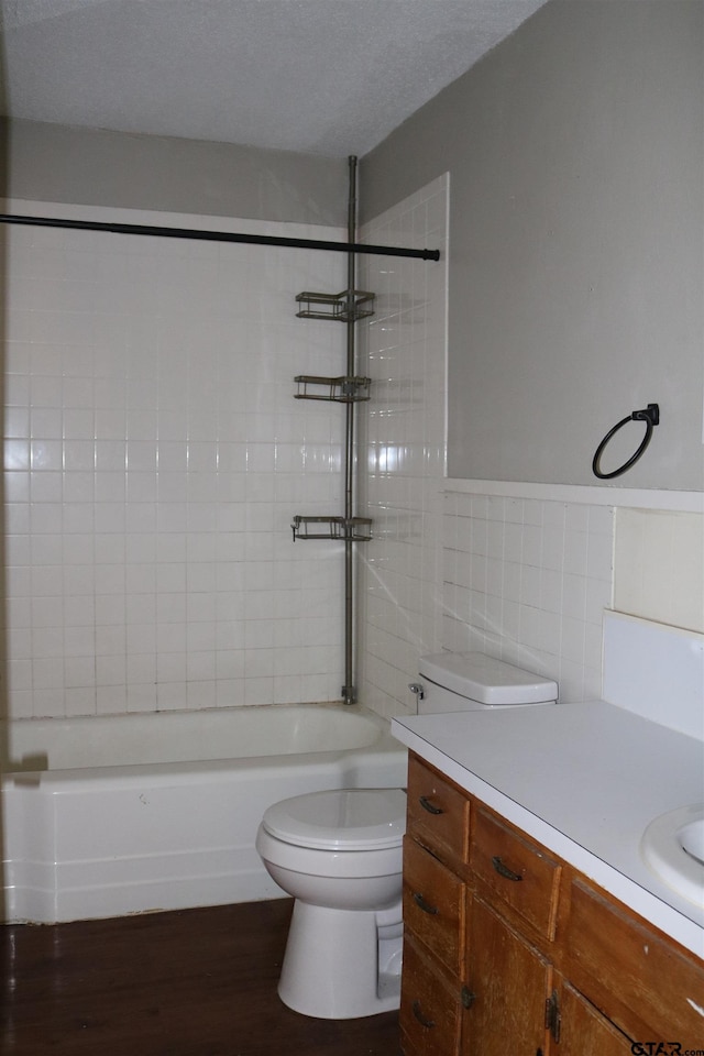 full bathroom with vanity, hardwood / wood-style flooring, tiled shower / bath combo, toilet, and tile walls