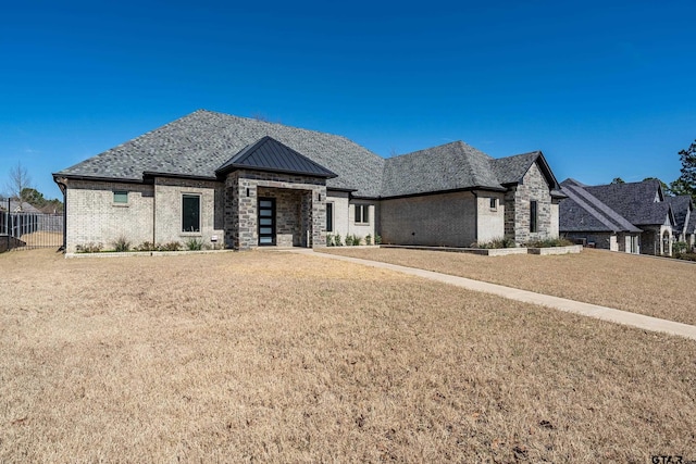 view of front facade with brick siding, a standing seam roof, fence, metal roof, and a front lawn