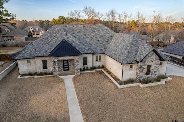 view of front of home with stone siding, a front yard, fence, and roof with shingles