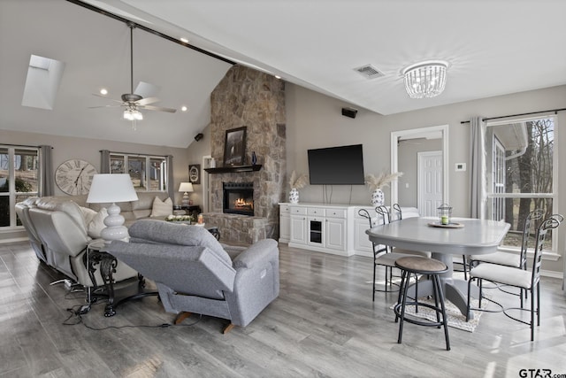 living room featuring ceiling fan with notable chandelier, visible vents, wood finished floors, and a stone fireplace